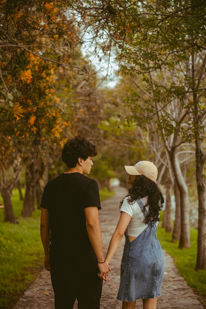 A young couple holding hands on a tree-lined path, creating a romantic and serene atmosphere.
